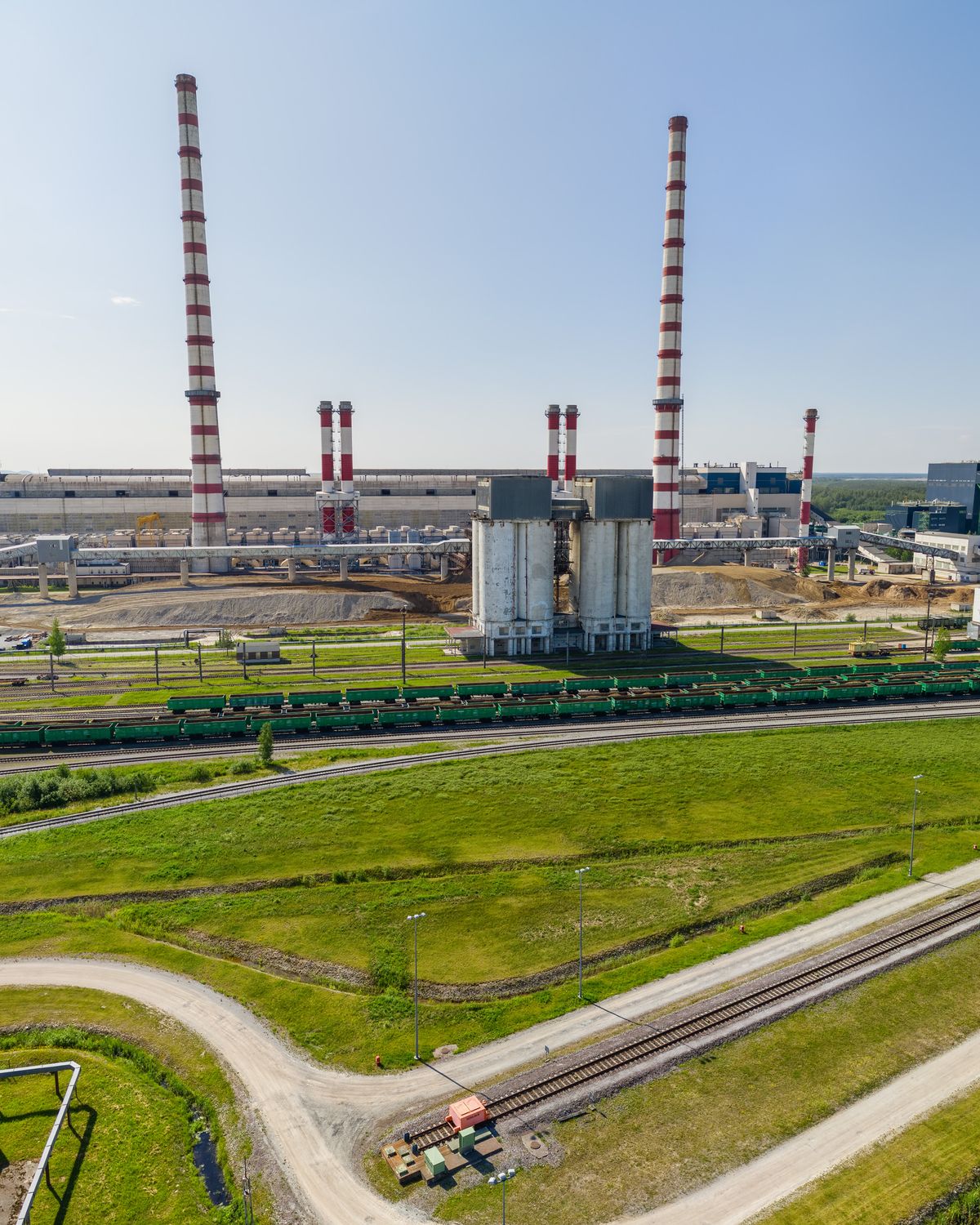 An oil-shale industrial site in Estonia from the air: red-and-white chimneys and grey silos beyond green fields and a railway lined with tank wagons