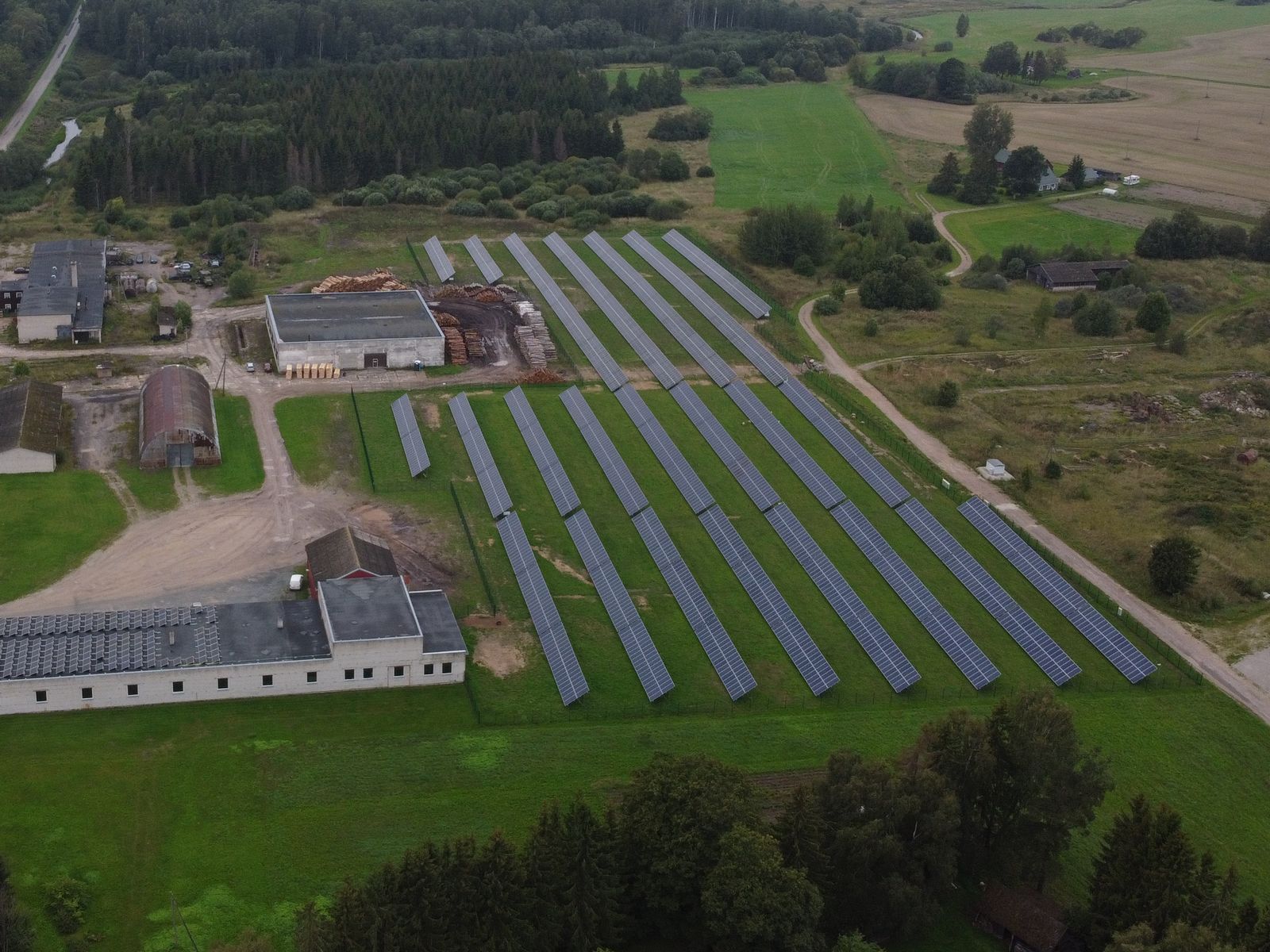 Rows of ground-mounted solar panels beside farm buildings in Voore village, seen from a drone