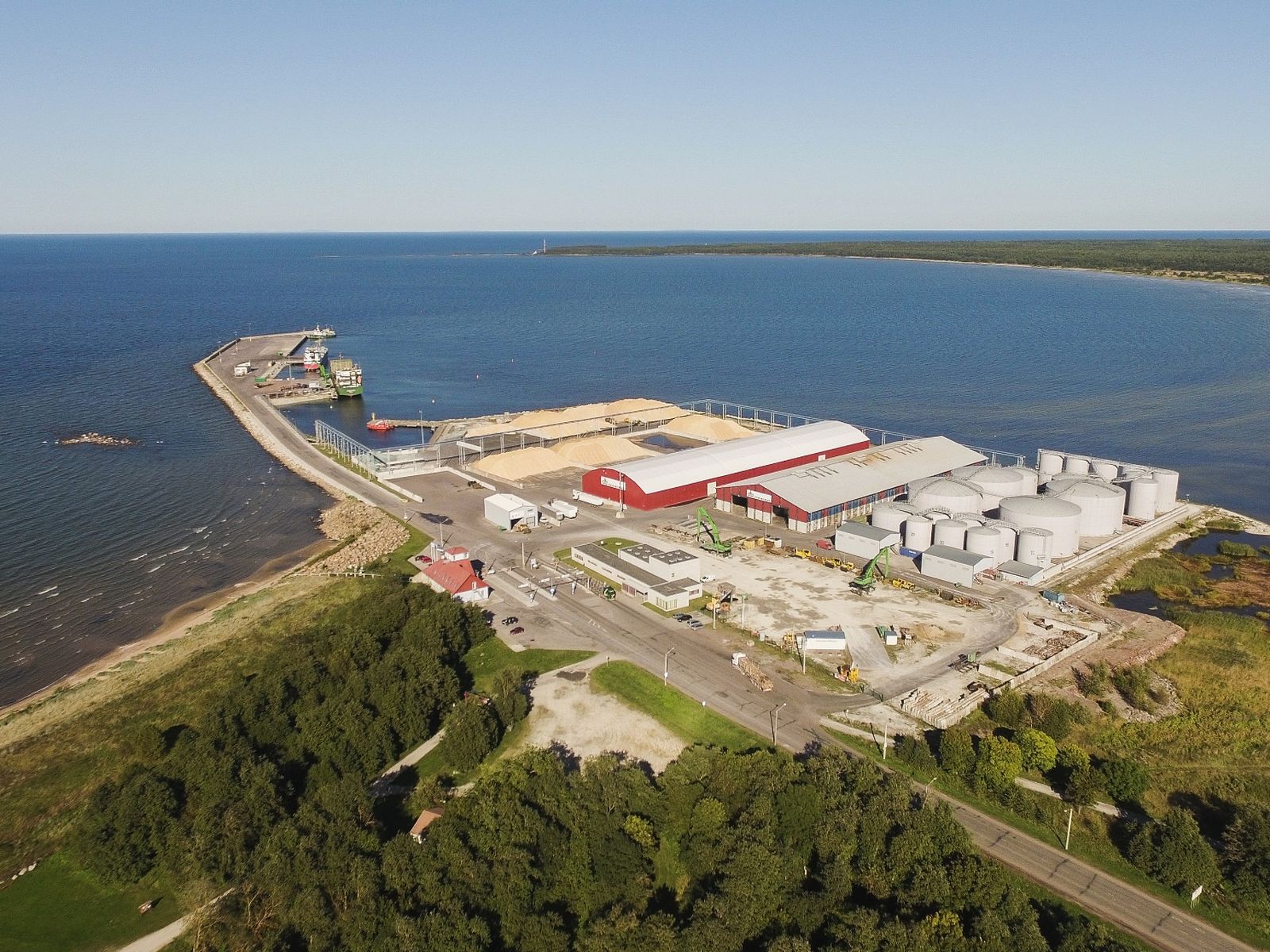 The port of Kunda from the air: open storage heaps, red-roofed warehouses, white tanks and loading machines on a pier