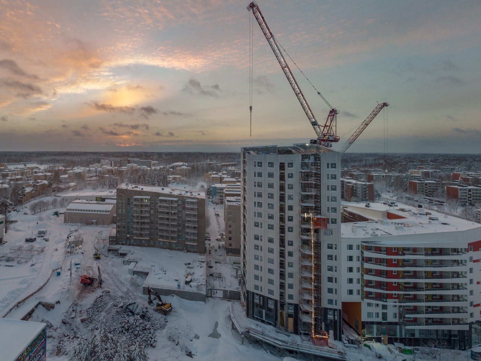 A tower block going up under a crane on a snowy building site at dusk, seen from the air