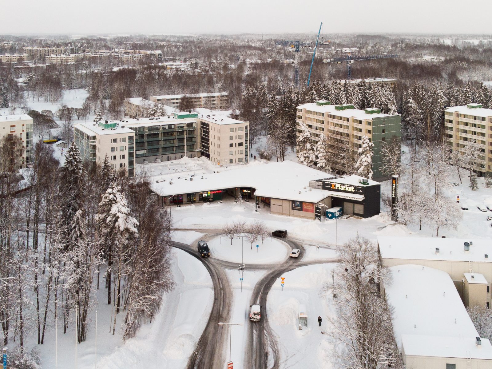 A snowy road and roundabout among apartment blocks, one car driving through