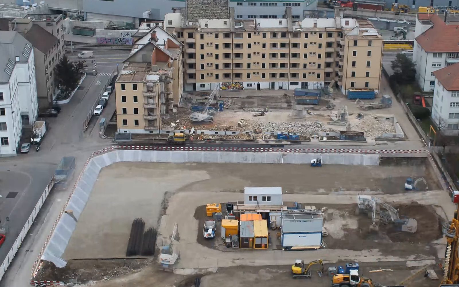 A building site in Zurich in 2020 seen from a roof: an empty pit, with an old block half torn down behind it