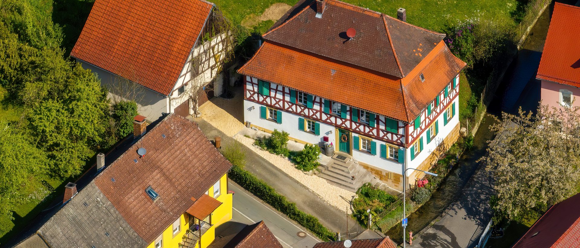 Neighbouring village houses from the air: tiled roofs, chimneys, a half-timbered house and the lane between them