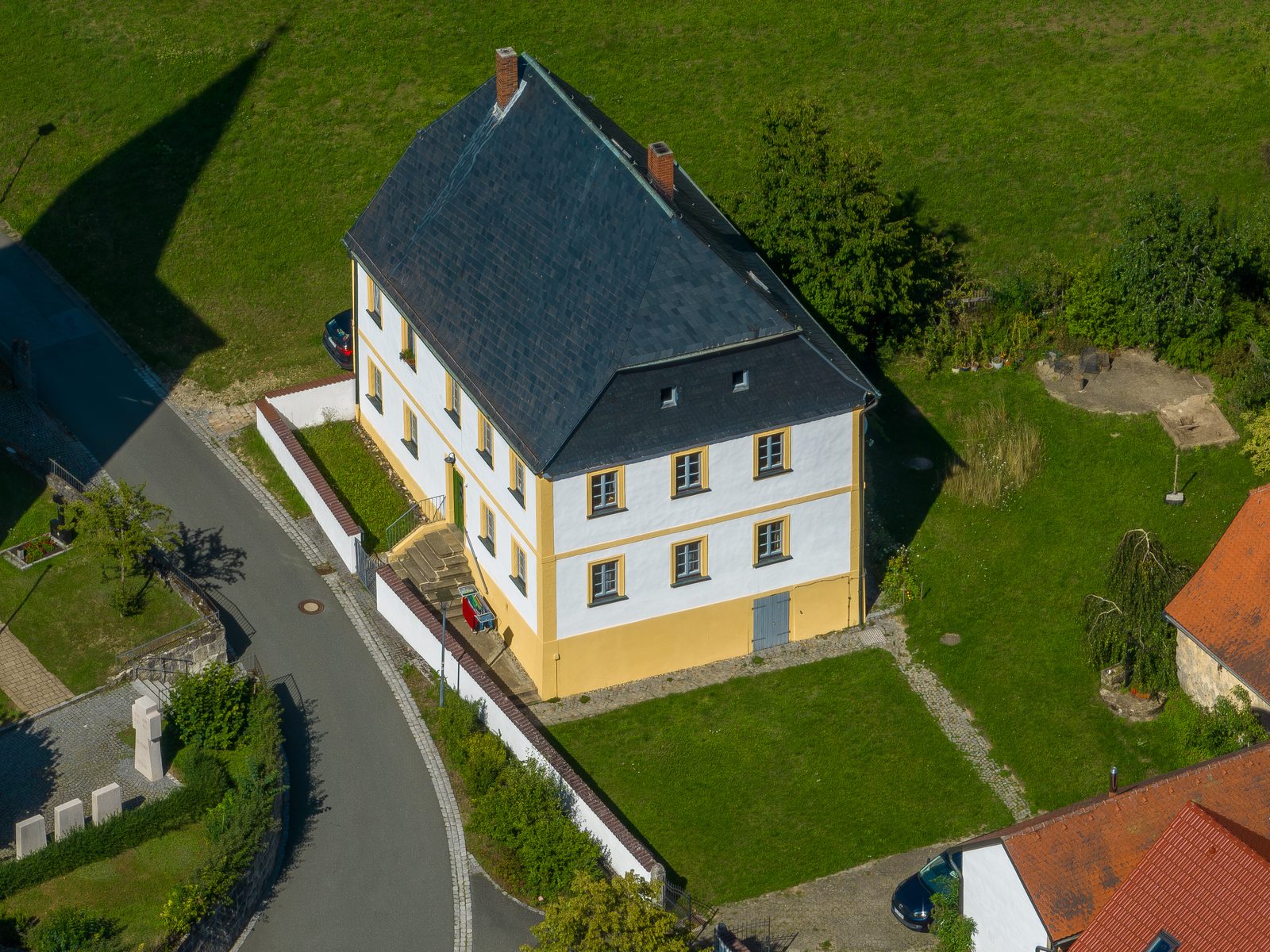 A two-storey house with a slate roof and two chimneys, seen at an angle from the air