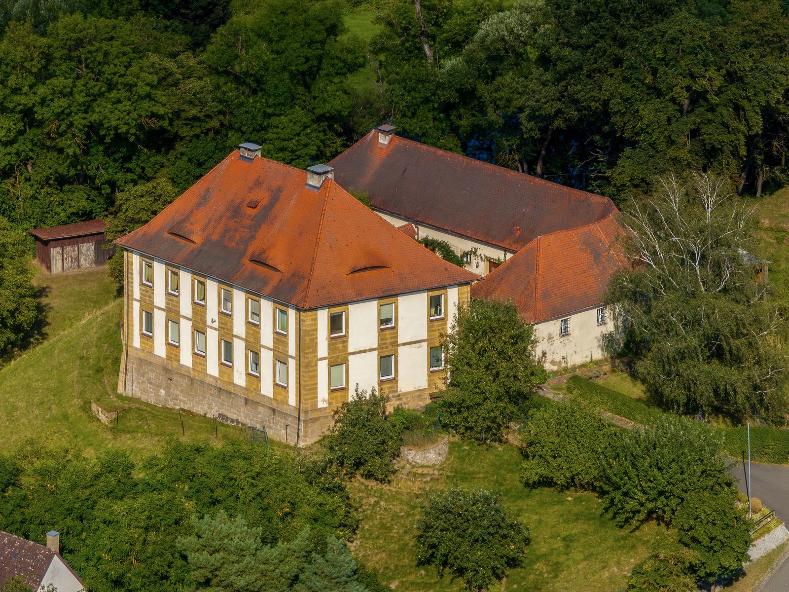 A weathered tile roof with two chimneys and small dormers on a large old house, seen from a drone in evening light
