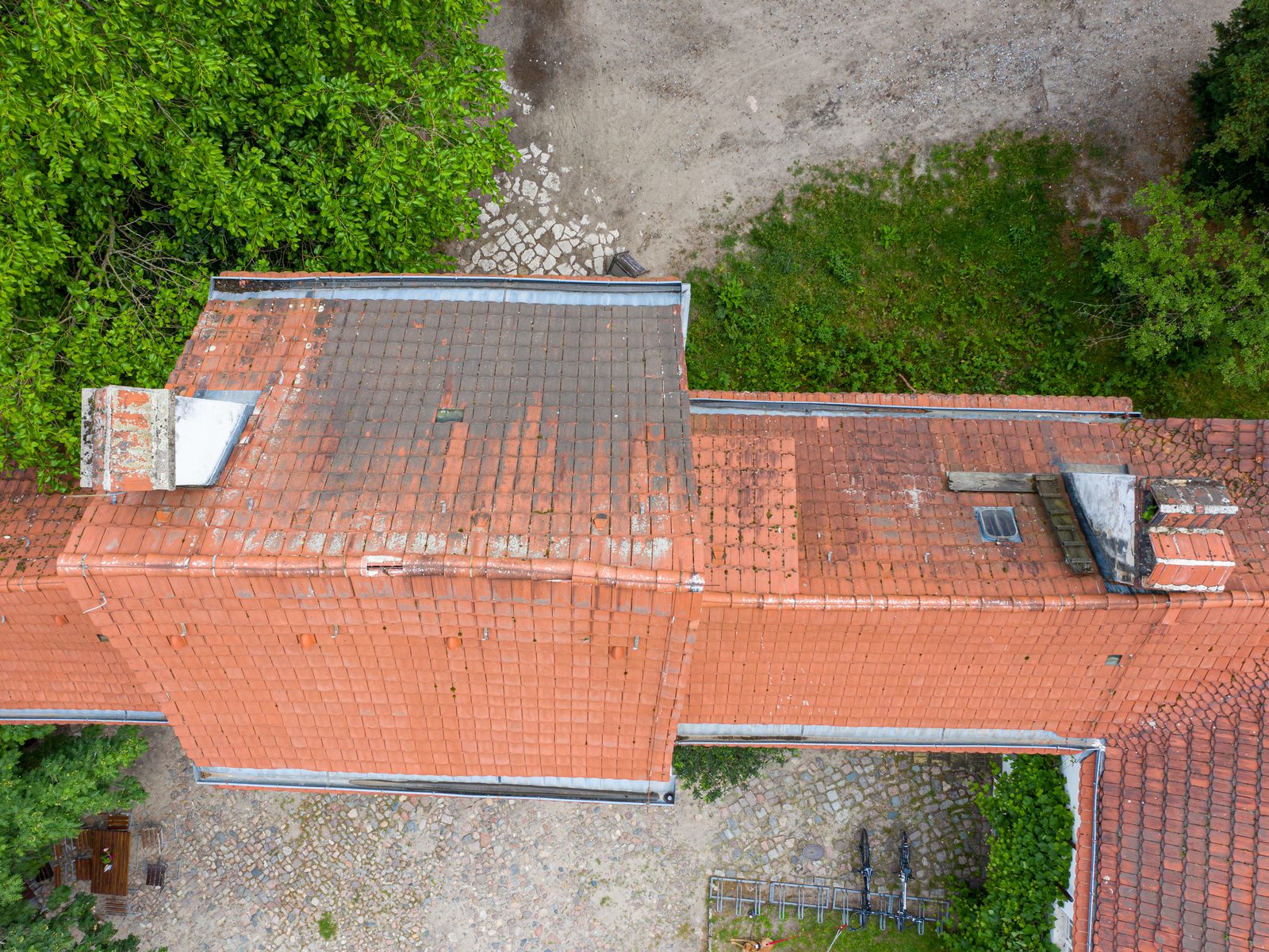 A tiled roof from straight above: chimneys, skylights, moss on the tiles and a gutter along the edge